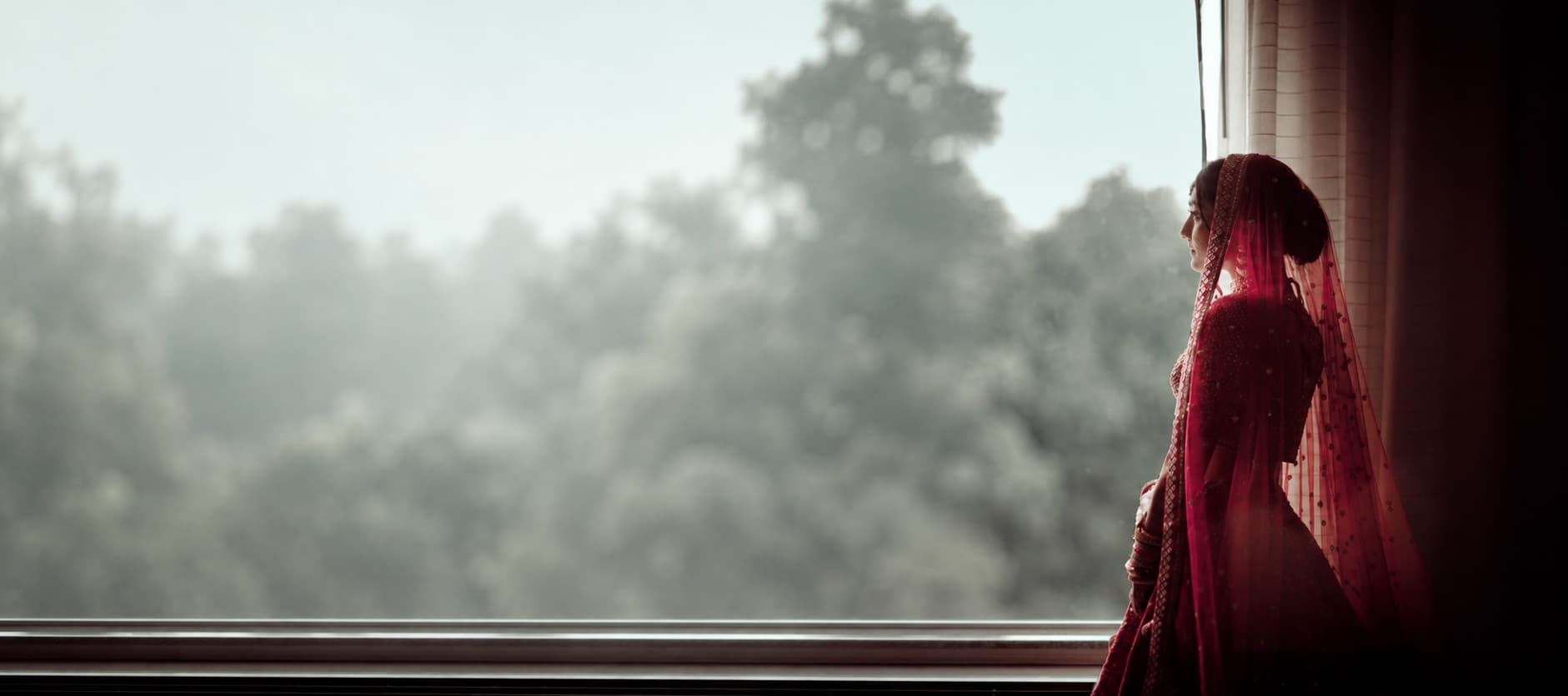 A bride in red at a window, in the morning light
